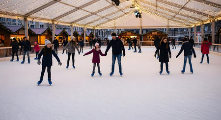 A group of people, including adults and children, are seen ice skating on a rink. They are dressed in warm winter clothing, enjoying the activity.の素材