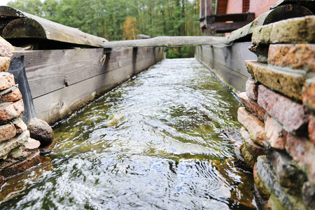 Water flows through a gutter made of wood and bricks against the background of forest and natureの写真素材