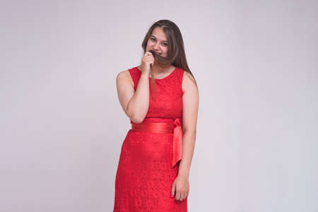 portrait of a beautiful brunette girl on a white background in a dress in different poses with different emotions. She is standing right in front of the camera smiling and looking happyの写真素材