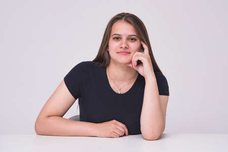 I listen carefully to you. Portrait of a beautiful manager girl on white background at a table. She sits right in front of the camera smiling and looks happyの写真素材