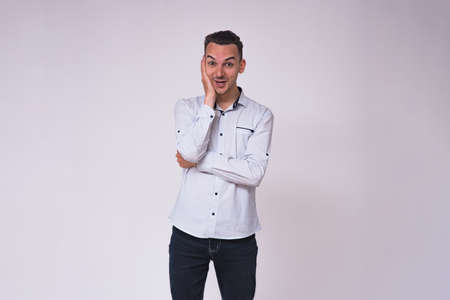 portrait of a cute young brunette man on a white background in different poses with different emotions. He stands directly in front of the camera and shows different emotionsの写真素材