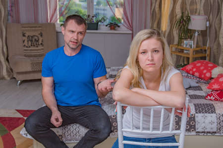 family relationships. Portrait of husband and wife: family quarrels, problems, family difficulties, family relationships in the room. They sit in front of the camera and look unhappyの写真素材