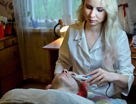 Beautician in the spa salon does massage device with mask. Photo of the face of a woman patient