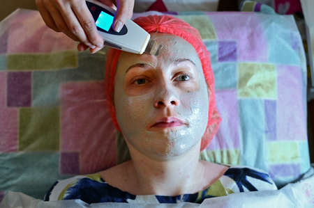 Photo of the face of a woman patient. Beautician in the spa salon does massage device with mask