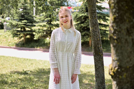 Full length portrait of a nice blonde girl smiling in a park. A Caucasian model in the background of trees stands in sunny weatherの写真素材