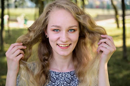 Portrait of a caucasian blonde girl smiling in a park. Photo of a pretty young woman with beautiful...