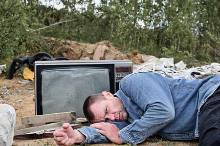 The model is lying on the ground and looking at the camera. Photo of a homeless man on the...