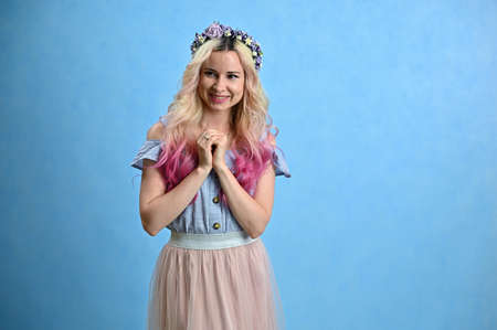 Blonde colored hair model smiling posing in studio on a blue background. Horizontal portrait of a...