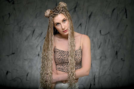 Portrait of a caucasian fashionable woman with afro dreadlocks long hair in studio. Pretty model posing on a gray background standing right in front of the camera.の写真素材