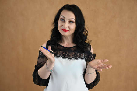 A close-up portrait of a pretty model talking on a beige background. A brunette woman is standing with a smile in the studio.の写真素材