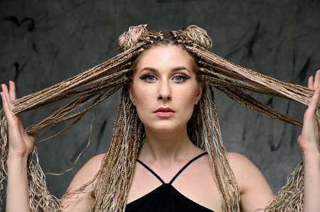 Pretty model posing on a gray background. Close-up portrait of a caucasian fashionable woman with long afro dreadlocks in studio.の写真素材