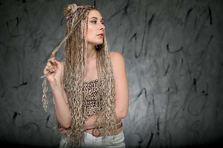 Portrait of a caucasian fashionable woman with afro dreadlocks long hair in studio. Pretty model posing on a gray background standing right in front of the camera.の写真素材