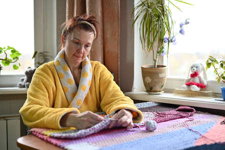 A portrait of a woman in a yellow dressing gown knits at home with her hands. The model is engaged...