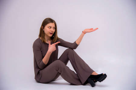 beautiful girl sits on the floor and shows a finger on a white backgroundの写真素材