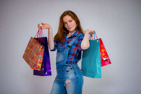 Red-haired young beautiful woman, happy smiling beautiful girl holding shopping bags with jeans suit on white backgroundの写真素材