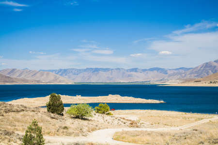Navy blue lake with a sandy foreground and hills behindの写真素材
