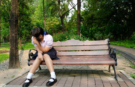 Thai student crying alone on the bench in the park の写真素材