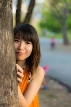 Cute Thai girl hiding behind the tree  の写真素材