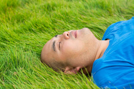 A fat man is lying on the soft green grass, relaxing with pleasureの写真素材