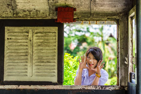 Cute Thai schoolgirl is making a surprise through the old window panel. Will anyone get frighten?の写真素材