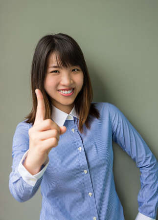 Asian office girl lifting her forefinger, showing determination in grey backgroundの写真素材