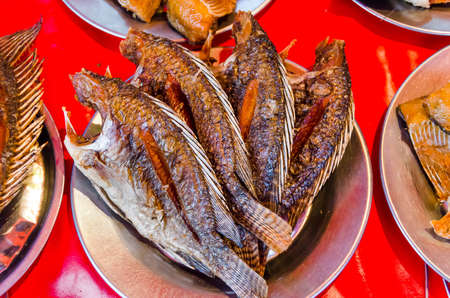 Fried tilapia fish on a silver plate with red background in Thailand open marketの写真素材