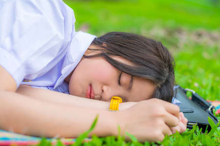 Cute Thai schoolgirl fall asleep during doing outdoor homework in the green fieldの写真素材