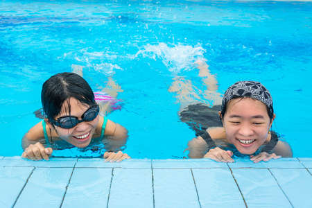 Two Asian girls are floating in the swimming pool by splashing their legs for warming upの写真素材