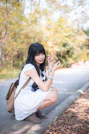 A cute Asian Thai girl is sitting and holding a dry leaf and making eye contactの写真素材