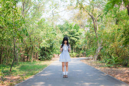 A cute Asian Thai girl is standing on a spring forest path aloneの写真素材