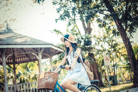Cute Asian Thai girl in vintage clothing is riding a bicycle, in the sunny summer park in soft Japanese tone.の写真素材