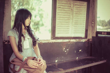 Cute Asian Thai girl in vintage clothes is waiting alone in an old bus stop in bright vintage color toneの写真素材