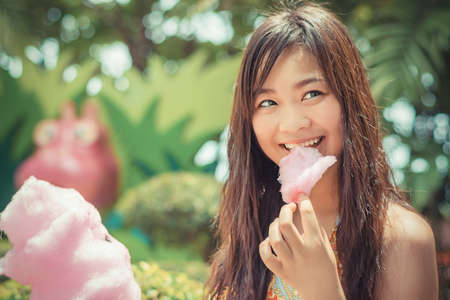 Cute Thai girl is eating pink candyfloss with joy in vintage colorの写真素材