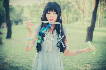 Cute Asian Thai girl is blowing a soap bubbles in the park in dreamy color