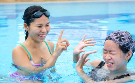 Two Asian girls are flicking water to one another in the swimming pool with happy expressionの写真素材