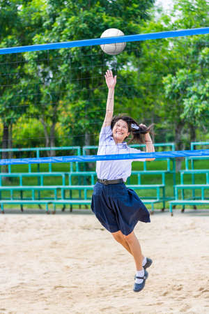 Cute Thai schoolgirl is playing beach volleyball in school uniform. Focus on the model face.の写真素材