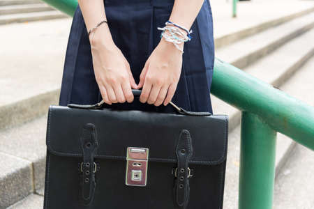 Body and hands of cute Asian Thai high schoolgirls student in school uniform holding black leather bag in education fashion conceptの写真素材