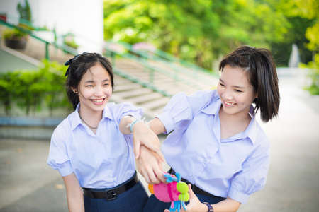 Cute Asian Thai high schoolgirls student couple in school uniform are having fun playing chasing and catching a doll with her student friend in a happy smile face expressionの写真素材
