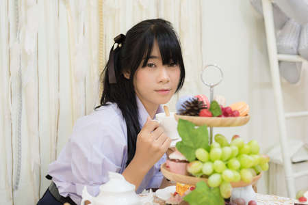 Cute Asian Thai high school girl in uniform in food decoration restaurant decoration with teacup in her hand in schoolgirl fashion concept.
の写真素材