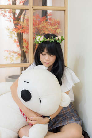 Cute Asian Thai teenage girl with fashionable clothes and flower tiara sitting and hugging fluffy teddy bear doll in the corner of the Japanese style room in fashion recreation concept.の写真素材