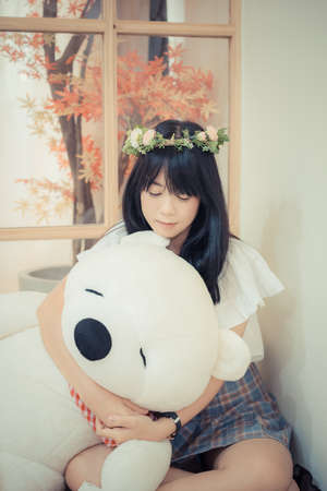 Cute Asian Thai teenage girl with fashionable clothes and flower tiara sitting and hugging fluffy teddy bear doll in the corner of the Japanese style room in vintage childhood fashion recreation concept.の写真素材