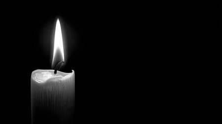 A single lit candle with a bright flame illuminates a dark background. The image features a high-contrast, monochromatic palette, emphasizing the interplay of light and shadow. The composition likely evokes themes of hope, spirituality, or commemoration, suitable for various visual communication projects.の素材