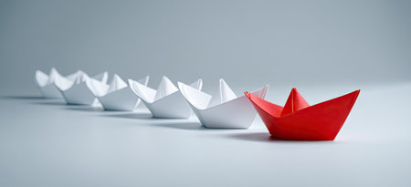 A single red paper boat stands out from a line of white paper boatsの素材