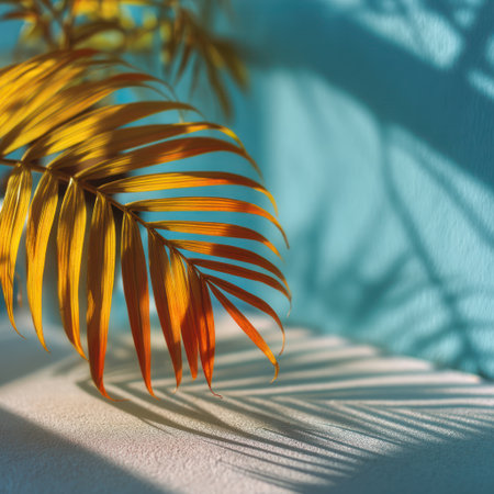 A close-up captures a golden palm leaf casting shadows against a light blue wall. The composition features a strong interplay of light and shadow, with a focus on textures and shapes. This image might be suitable for various commercial or editorial applications such as design, decoration, or environmental themes.の素材