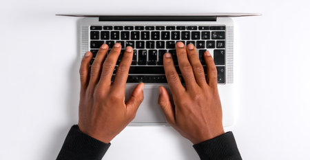 An overhead shot reveals hands typing on a laptop keyboard. The image highlights the hands and keyboard against a white background. It displays a workspace setting with attention to detail and texture. Suitable for illustrating technology, business, or creative content in various editorial or commercial applications.の素材