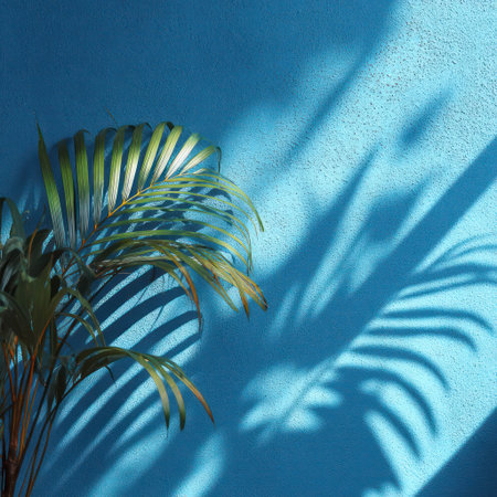 An overhead shot depicts palm leaves against a vivid turquoise wall. The foliage, in shades of green and brown, creates shadows on the textured surface. The image exhibits clean lines and a modern style. The graphic could be used for various design, decorative, or artistic purposes.の素材