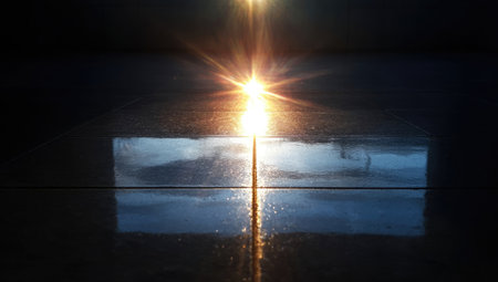 A radiant light source shines brilliantly through a rectangular opening, contrasting with the encompassing darkness. The scene displays a stark composition, with reflections adding a textural element. This image may be suitable for illustrating concepts of illumination or transition for various editorial or commercial applications.の素材