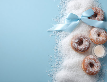 An overhead shot reveals donuts arranged on a textured, snow-like surface. A light blue ribbon and a small candle sit near the donuts against a plain blue backdrop. The image utilizes soft lighting, creating a calm visual. This arrangement lends itself to various commercial and editorial applications.の素材