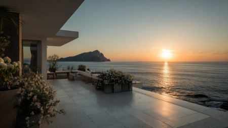 A luxury home overlooks the ocean as the sun sets, casting warm light on the water. The composition highlights a modern building with a terrace adorned with floral arrangements. The image features a clear sky and the overall aesthetic suggests peacefulness with potential applications in travel or real estate.の素材