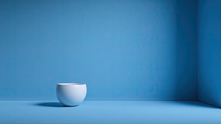 A minimalist white bowl rests on a vibrant blue surface, set against a matching backdrop. The image features strong directional lighting creating a prominent shadow. This composition uses clean lines and simple geometry. Suitable for various design projects, it can be used for advertising and marketing.の素材